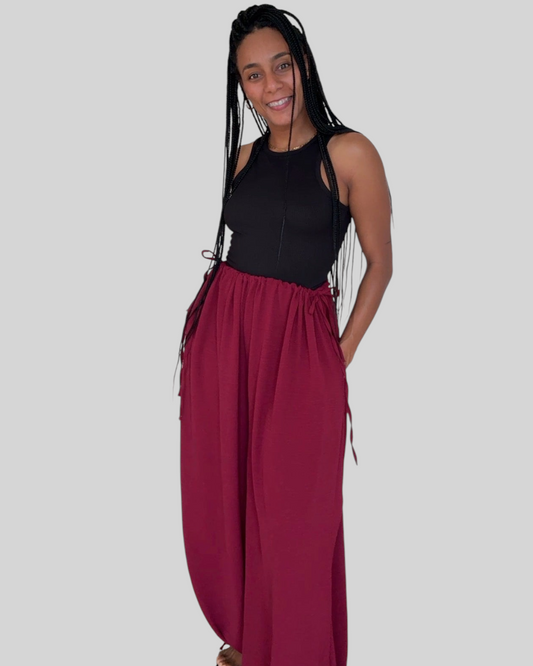 Modelo sonriente vistiendo el pantalón bombacho burdeos AFRA ATELIER con lazadas ajustables y bolsillos laterales