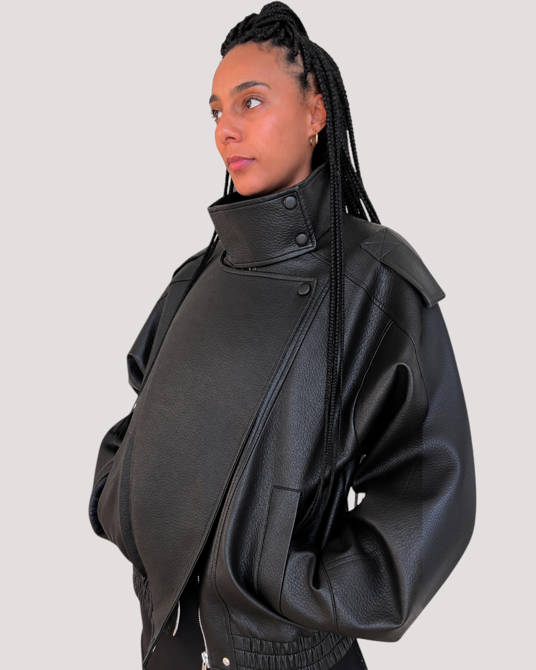 Modelo con chaqueta AFRA ATELIER de polipiel negra con cuello alto y diseño oversize sobre fondo blanco
