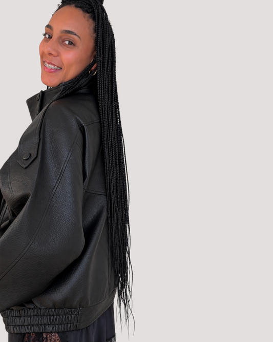 Mujer sonriente con trenzas luciendo una chaqueta de polipiel negra de AFRA ATELIER con diseño de hombreras