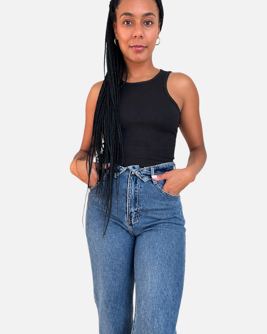Modelo con jeans de tiro alto AFRA ATELIER en mezclilla azul y top negro sin mangas sobre fondo blanco