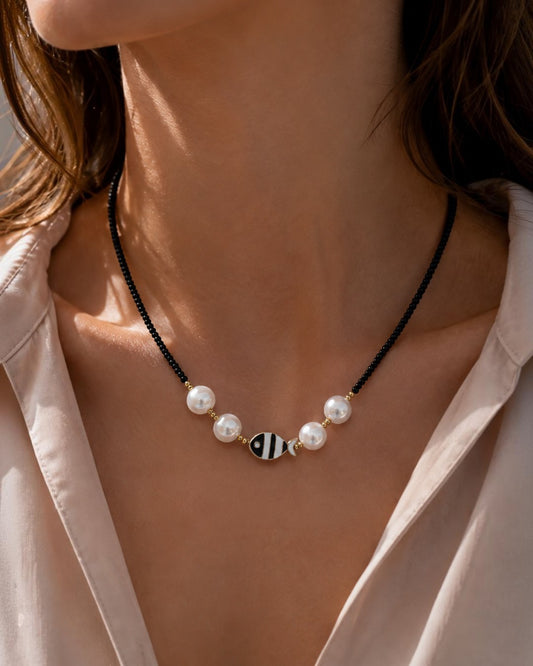 Collar Cala de A F R A A T E L I E R con cuentas negras, perlas blancas, detalles dorados y colgante de pez en acero